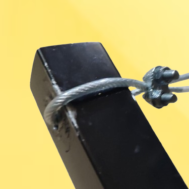 Close-up of a black metal post secured with a gray steel cable, set against a bright yellow background.